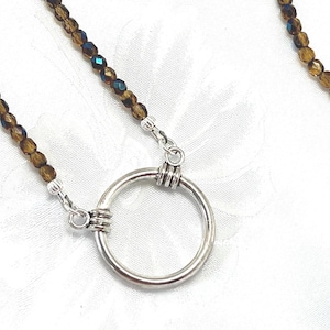 May include: A necklace featuring a circular silver-toned pendant attached to a chain of small, translucent brown faceted beads. The pendant is connected to the beaded chain by silver-toned metal findings, creating a simple, continuous design.