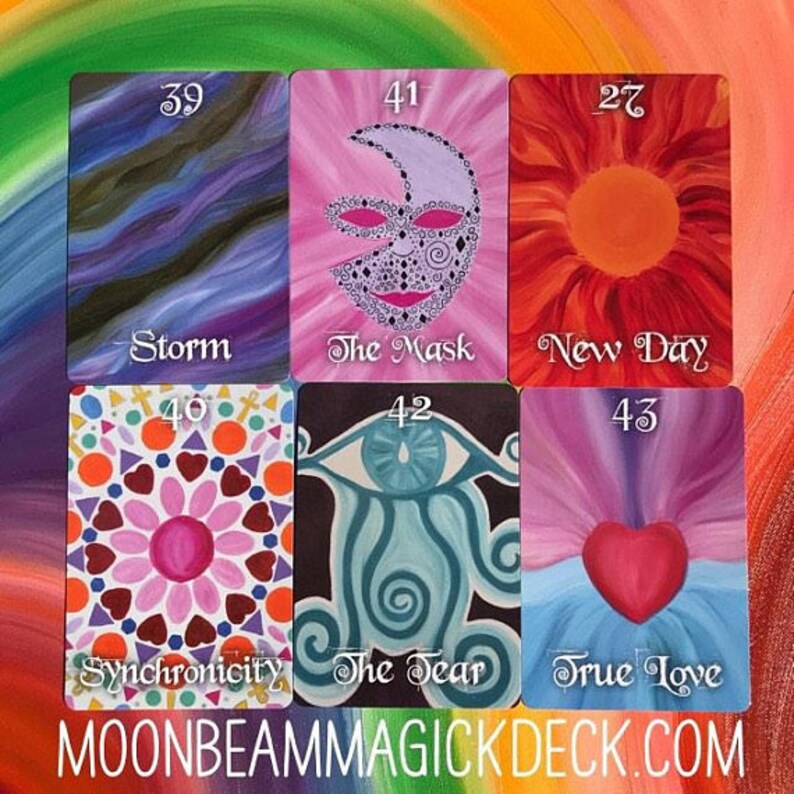 May include: A collection of six colorful tarot cards. The cards feature various illustrations, including a mask, a heart, and an eye. Each card has a title and a number. The website address MOONBEAMMAGICKDECK.COM is at the bottom.