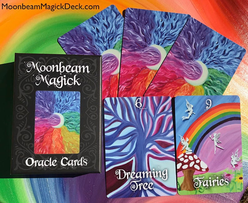 May include: A black box of "Moonbeam Magick Oracle Cards" with a colorful illustration of a crescent moon and rainbow. Several cards are fanned out, featuring vibrant art of trees, fairies, and rainbows. The website MoonbeamMagickDeck.com is visible at the top.