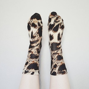 May include: A pair of brown and white patterned socks with a sheer fabric. The socks are worn on a person's legs.