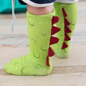 May include: Green and red dinosaur socks with a tail on the back of the socks.
