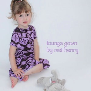 May include: A young girl wearing a purple and brown patterned lounge gown sits on a white background with a gray elephant stuffed animal. The text "lounge gown by mel henry" is written in purple on the white background.