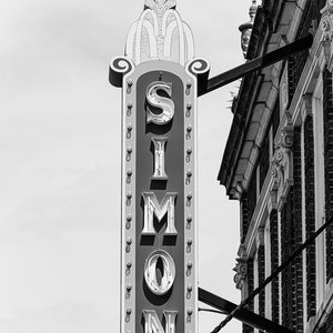 May include: Black and white photo of a vintage sign with the word "SIMON" in large, white letters with a decorative border.