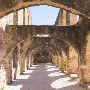 Puede incluir: Un largo y estrecho pasillo con una serie de arcos de piedra. Los arcos est&aacute;n hechos de piedra toscamente labrada y est&aacute;n sostenidos por pilares. El pasillo est&aacute; iluminado por la luz del sol que entra por la parte superior de los arcos. El suelo est&aacute; hecho de grava.