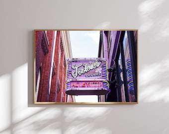 May include: A framed print featuring a vintage neon sign for "Tootsie's Orchid Lounge" in Nashville, Tennessee. The sign is purple with yellow and white accents, set against a backdrop of brick buildings and a blue sky.