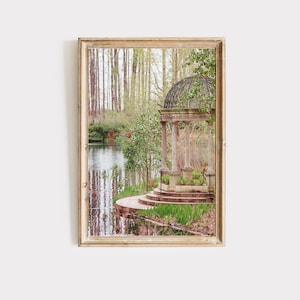 May include: A white gazebo with a black metal roof sits on a stone platform overlooking a still pond. The gazebo is surrounded by lush greenery and trees.