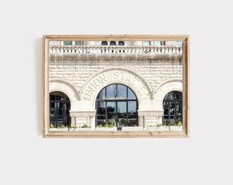 May include: A framed photograph of a building facade. The building is made of light-colored stone and features arched doorways and windows. The words "UNION STATION" are arched above the central doorway. The photograph is in a wooden frame.