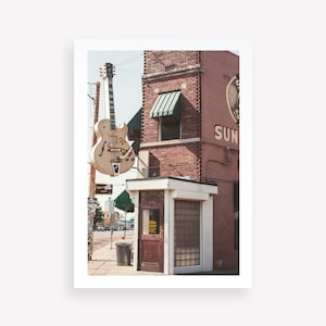 May include: A large, white electric guitar is mounted on the side of a brick building. The building has a green awning and the words "Sun Studio" in large, red letters. There is a small, white building with a wooden door and a glass window.