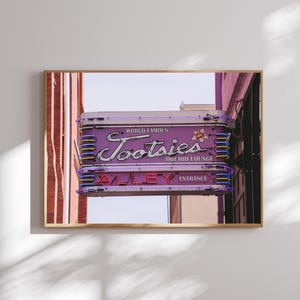 May include: A neon sign with purple and white lettering that reads "World Famous Tootsies Orchid Lounge Alley Entrance". The sign is mounted on a building with red brick walls.