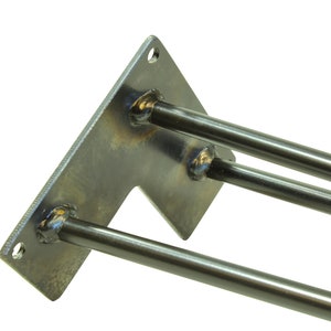 May include: A metal bracket with three welded steel rods extending from it. The bracket is rectangular with a cut-out on one side. The rods are all the same length and are welded to the bracket at a 90-degree angle.