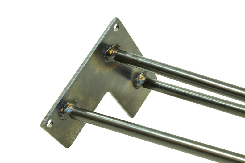 May include: A metal bracket with three welded steel rods extending from it. The bracket is rectangular with a cut-out on one side. The rods are all the same length and are welded to the bracket at a 90-degree angle.