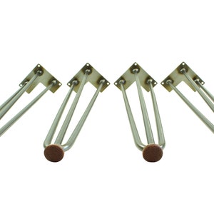 May include: Four silver metal hairpin table legs with brown felt pads on the bottom. The legs are designed to be attached to a table top.