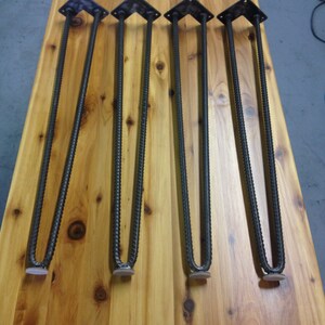 Puede incluir: Cuatro patas de horquilla de metal negro con almohadillas de fieltro blanco en la parte inferior. Las patas est&aacute;n dispuestas en una fila sobre una superficie de madera.
