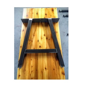 May include: A wooden table top with a black metal A-frame base. The table top is made of light wood with a natural finish.