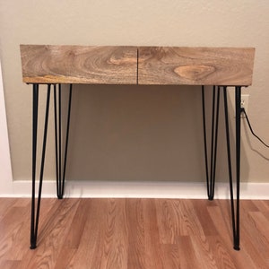 May include: A wooden desk with two drawers and black hairpin legs. The desk is made of light brown wood with a natural wood grain.