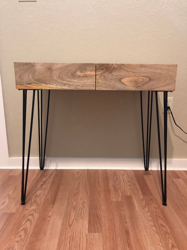 May include: A wooden desk with two drawers and black hairpin legs. The desk is made of light brown wood with a natural wood grain.