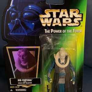 Op de afbeelding: Een Star Wars-actiefiguur van Bib Fortuna, een personage uit het Star Wars-universum. De figuur draagt een blauwe robe en een witte nekstuk. De figuur houdt een blaster in zijn rechterhand. De figuur is verpakt in een plastic blisterverpakking met een groene achtergrond. De verpakking bevat de tekst "Star Wars The Power of the Force" en "Collection 2".