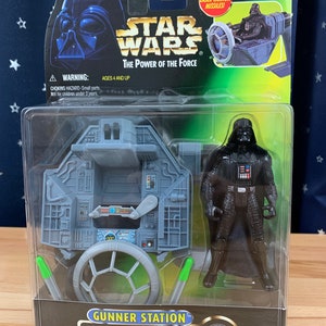 May include: A Star Wars action figure set featuring Darth Vader and his TIE Fighter. The set includes a gunner station with a rotating cannon and two green laser missiles. The packaging features the Star Wars logo and the words "The Power of the Force".