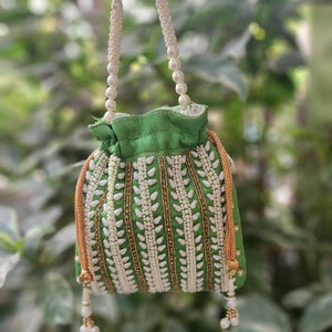 May include: A green drawstring bag with a white pearl and gold bead embellishment. The bag has a white pearl handle.