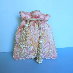 May include: A pink silk drawstring bag with gold embroidery and pearl embellishments. The bag has two pearl tassels.