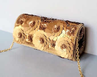 May include: A gold-colored clutch with a chain strap, covered in sequins and embellished with floral designs. The bag features a beaded border and a gold chain strap. The floral design is made of large, circular sequins.