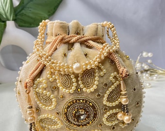 May include: A cream-colored velvet drawstring bag with gold and pearl embellishments. The bag is decorated with a large floral design and has a tassel.