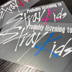Może przedstawiać: Trzy naklejki winylowe na przezroczystych arkuszach podkładowych. Każda naklejka zawiera biały napis "Probably listening to" nad stylizowanym białym napisem "Stray Kids". Cyfra 4 w słowie Kids jest w kolorze czerwonym, r&oacute;żowym lub niebieskim.