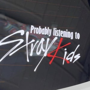 Może przedstawiać: Biało-czerwona naklejka winylowa umieszczona na ciemnej szklanej powierzchni. Tekst brzmi "Probably listening to" prostą białą czcionką, po kt&oacute;rym następuje słowo "Stray" dużym białym pismem odręcznym oraz "Kids" czerwono-białym pismem odręcznym.