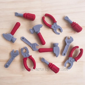 May include: A set of ten grey and red toy tools, including a hammer, wrench, pliers, and screwdrivers. The tools are arranged on a wooden surface.