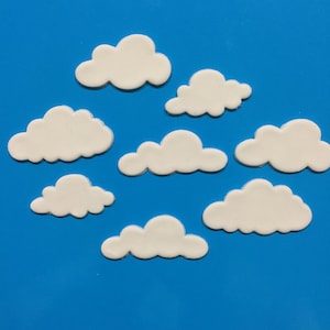 May include: Eight white cloud-shaped decorations are arranged on a bright blue surface. The clouds have a smooth, rounded design and vary in size. Suitable for craft projects or decorations with a weather or sky theme.
