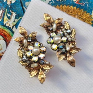 Puede incluir: Un par de pendientes de tono dorado con un diseño floral. Los pendientes presentan piedras de imitación de cristal iridiscentes, perlas falsas y hojas doradas.