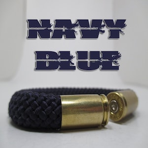 May include: A navy blue paracord bracelet with a brass bullet casing clasp. The bracelet is woven with a diamond pattern.