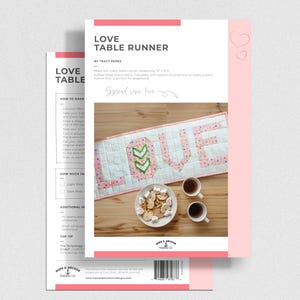 Könnte beinhalten: Ein rosa-weißes Tischläufermuster mit dem Wort "LOVE" in großen Buchstaben. Das Muster enthält Anweisungen und Illustrationen. Das Bild zeigt auch einen fertigen Tischläufer, einen Teller mit Keksen und zwei Tassen Kaffee.
