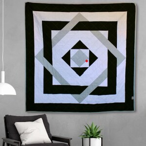 May include: A black and white geometric quilt with a red dot in the center. The quilt features a series of squares and diamonds within squares, creating a layered and intricate design.