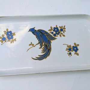 Könnte beinhalten: Rechteckige weiße Servierplatte mit einem blauen Vogel- und Blumendesign. Der Vogel hat blaue Federn mit goldenen Akzenten, die auf einem Ast sitzen. Blaue Blumen mit goldenen Blättern sind über die Platte verstreut. Goldener Rand.