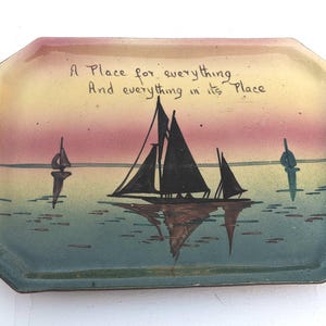 May include: A rectangular ceramic tray with a sunset scene and a sailboat silhouette. The tray has a green, yellow, and pink glaze and features the text "A Place for everything And everything in its Place".