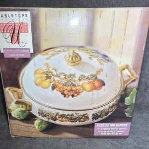 May include: A white Kensington Garden 10-inch covered buffet server with a lid and gold accents. The server features a fruit and floral design. The box reads "Tabletops Unlimited" and "Kensington Garden Collection."