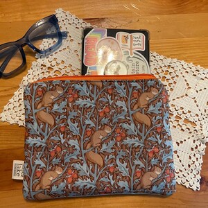 May include: A blue and brown zippered pouch with a squirrel and acorn pattern. The pouch is on a white crocheted doily. The text "The Lake District" is visible on the pouch.
