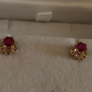 May include: A pair of gold earrings with red ruby stones set in a floral design.