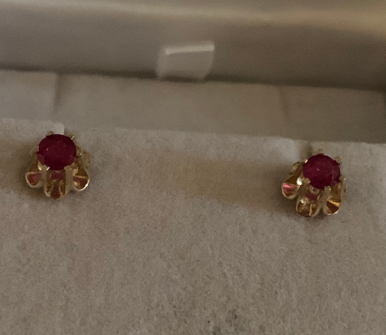 May include: A pair of gold earrings with red ruby stones set in a floral design.