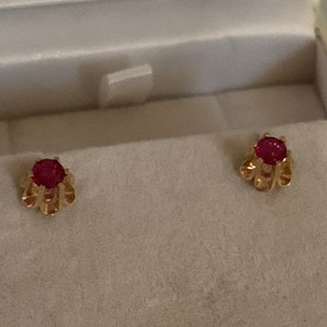 May include: A pair of gold earrings with red ruby stones set in a flower-shaped design.
