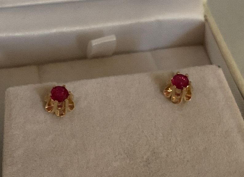 May include: A pair of gold earrings with red ruby stones set in a flower-shaped design.