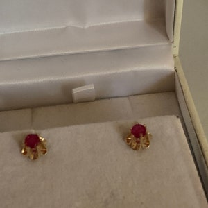 May include: A pair of gold earrings with small red gemstones set in a floral design.