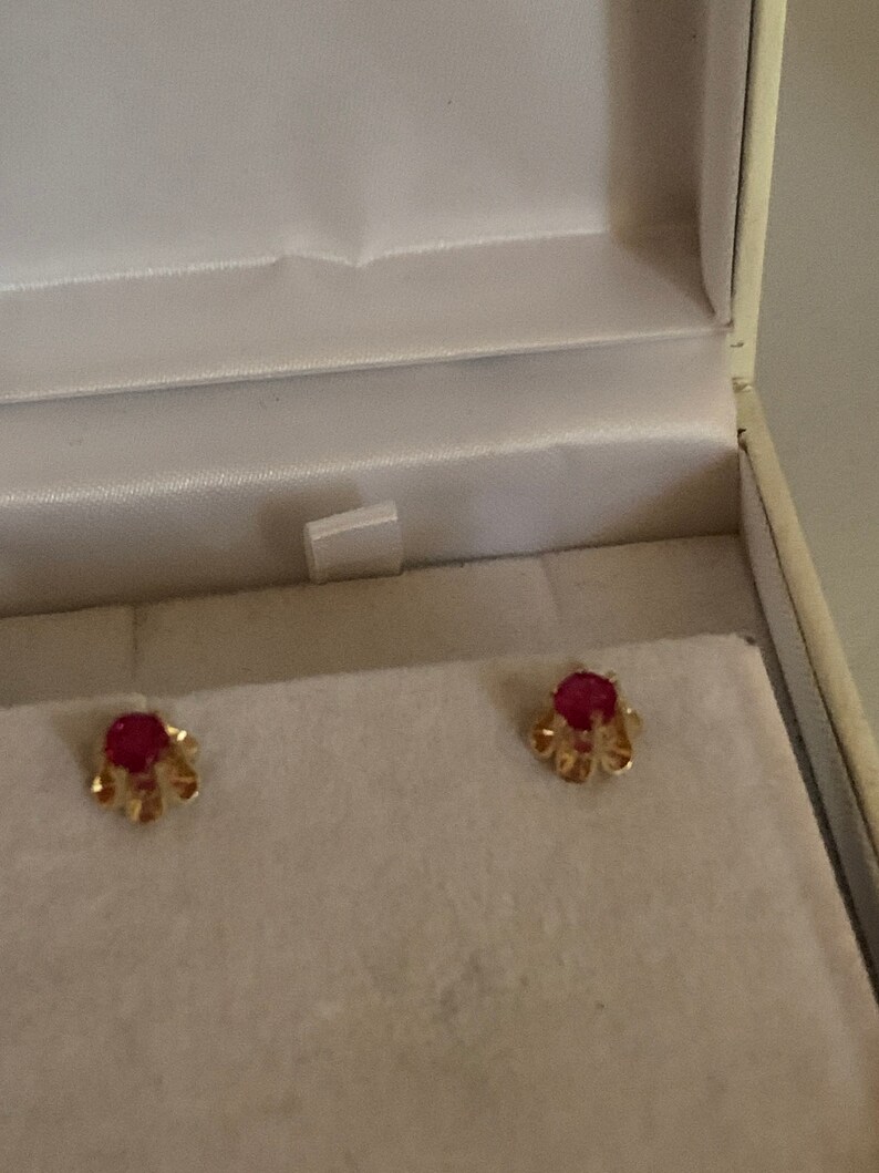 May include: A pair of gold earrings with small red gemstones set in a floral design.