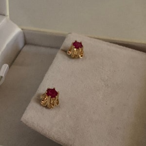 May include: A pair of gold earrings with red gemstone accents. The earrings are in a small box.
