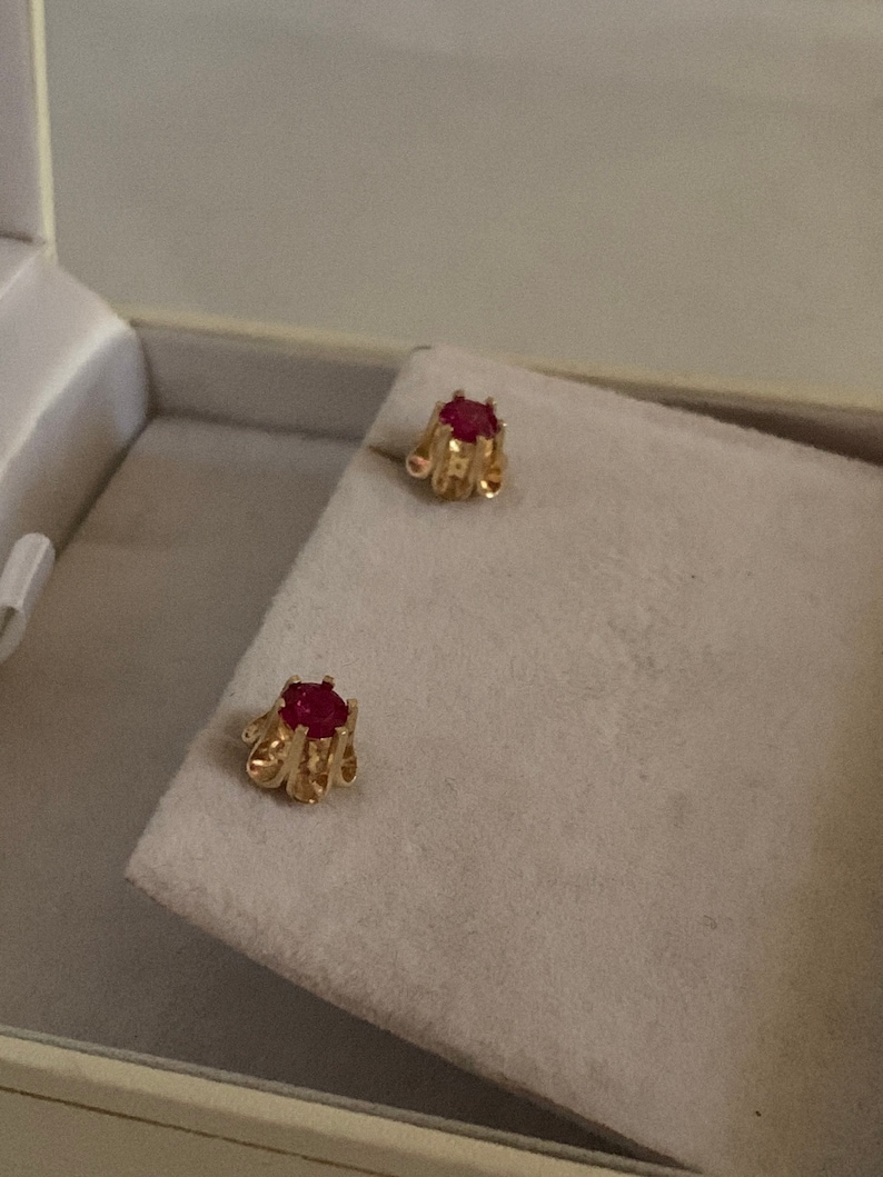 May include: A pair of gold earrings with red gemstone accents. The earrings are in a small box.