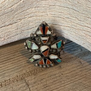 May include: A silver ring with a geometric design featuring a variety of colorful stones, including turquoise, red, black, and white.