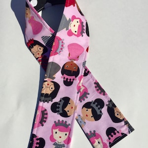 May include: Pink fabric strap with a black and white polka dot pattern on one side and a pink pattern of girls with crowns on the other side.