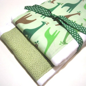 May include: A green and brown fabric baby burp cloth with a white polka dot ribbon tied around it. The fabric has a pattern of giraffes and leaves.