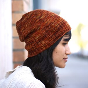 May include: A woman wearing a slouchy, orange and brown knitted beanie hat.